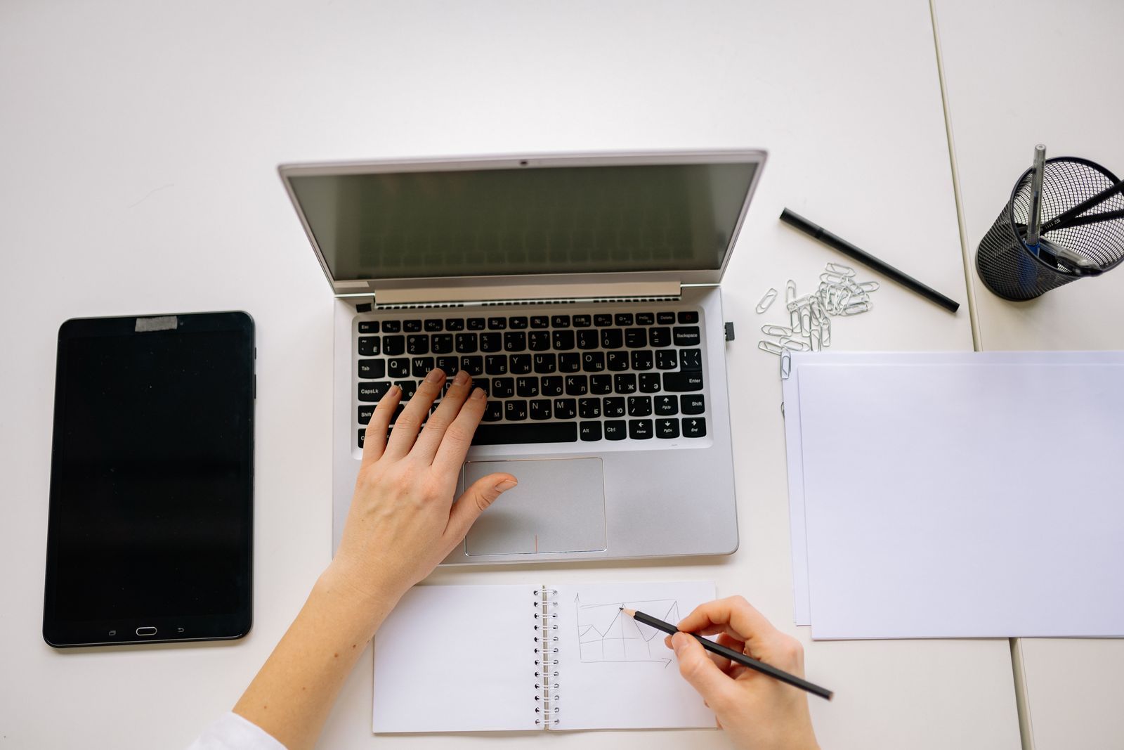 Vue de dessus d'un poste de travail: ordinateur portable, carnet et tablette.
