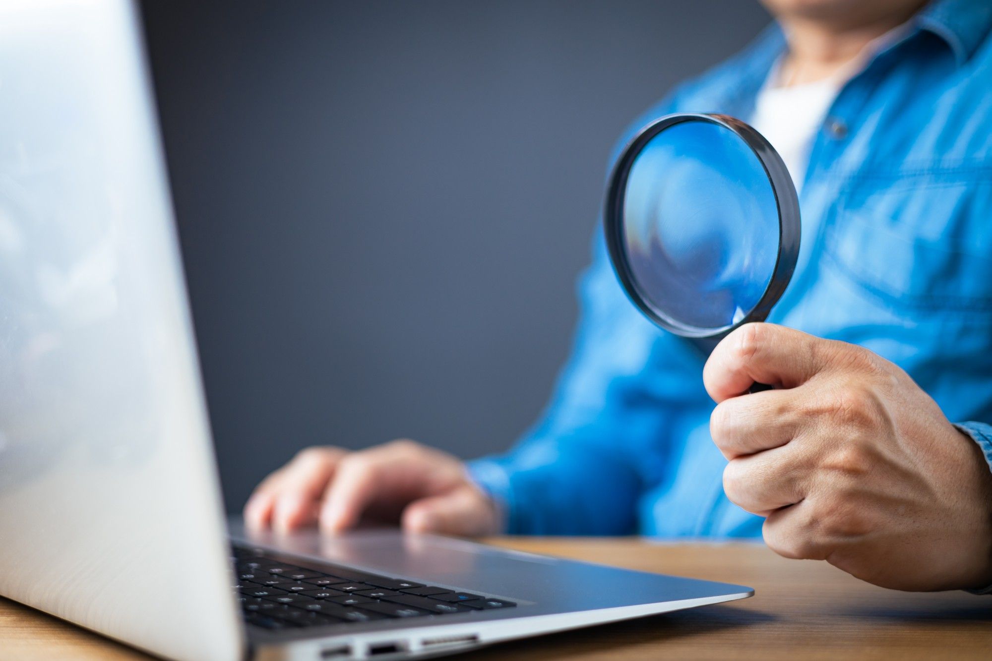 Personne examinant son ordinateur portable à la loupe, symbole du recensement des usages de l'IA.