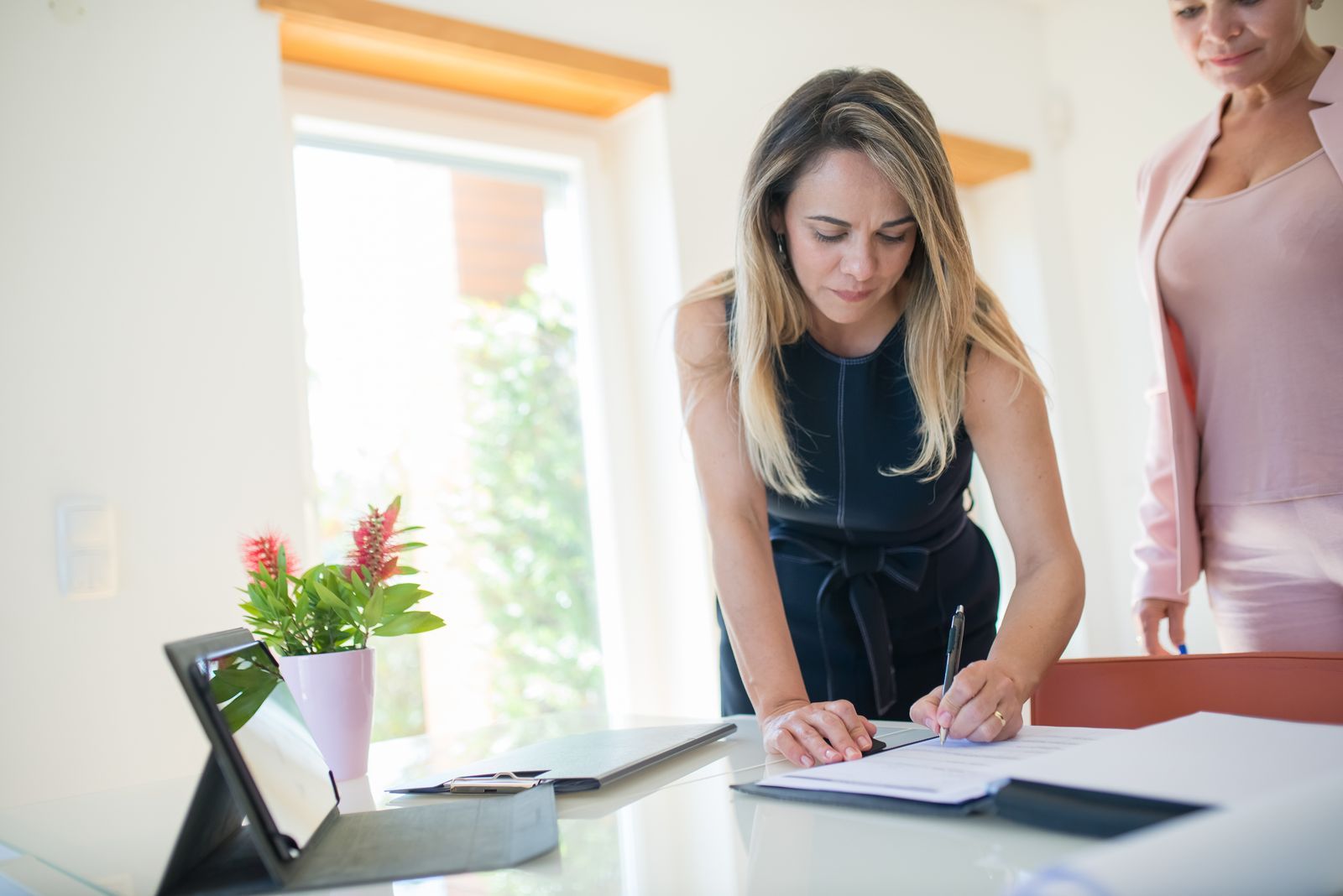 Une dirigeante signe un document, une tablette posée sur le bureau.